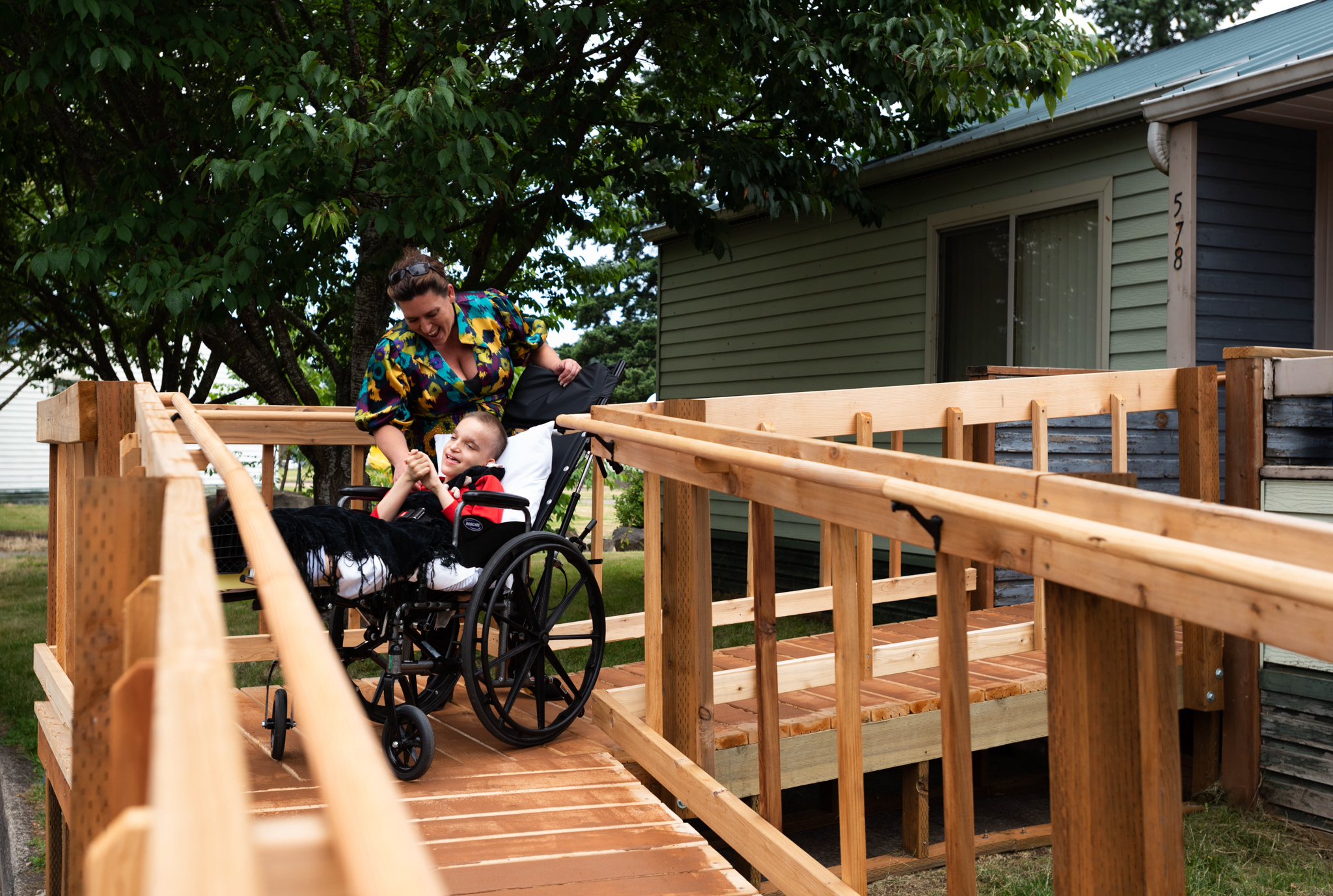 A boy smiles in his wheelchair, his caretaker is near by