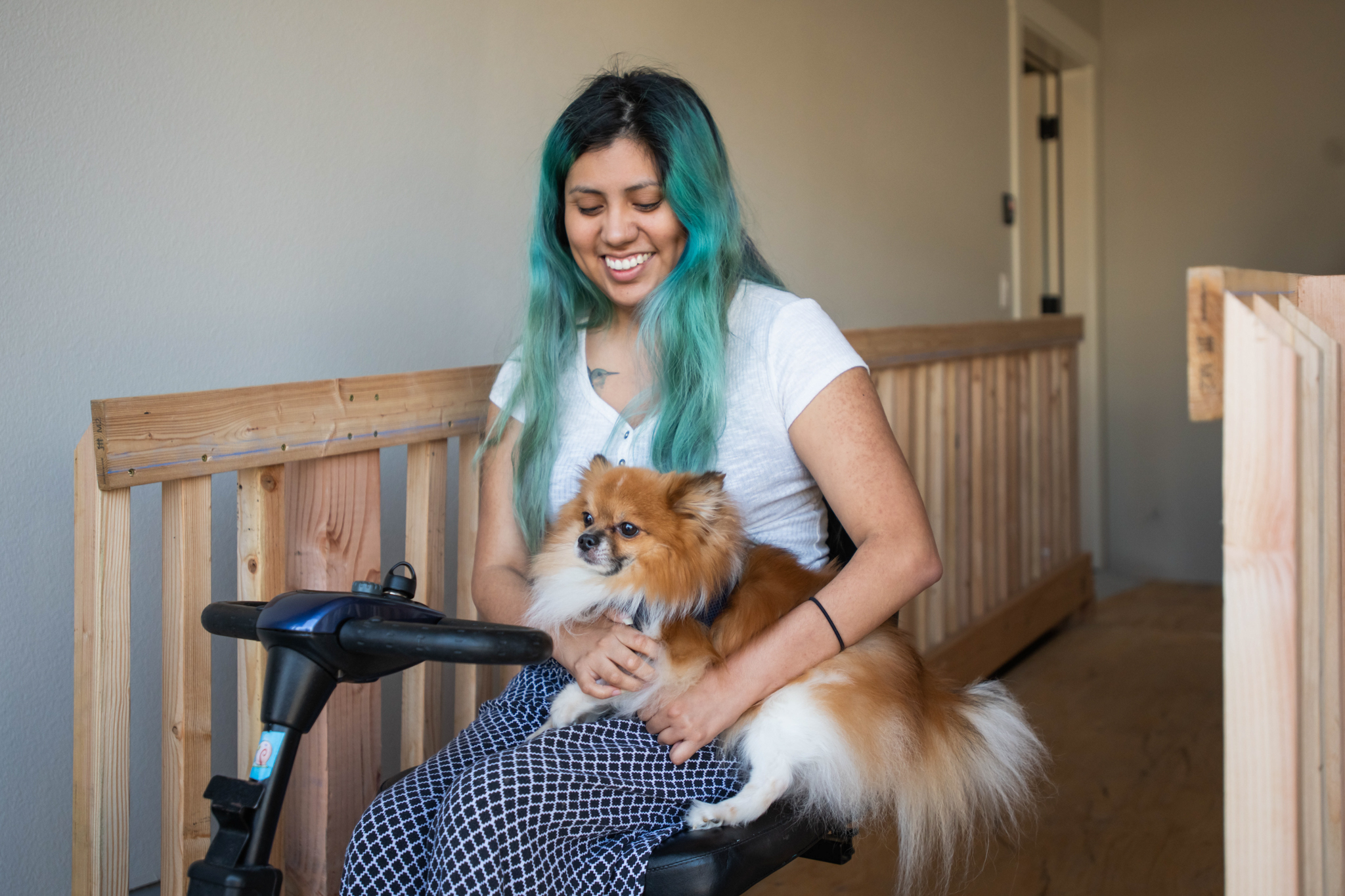 A woman who uses a power scooter smiles while holding her small dog in her lap